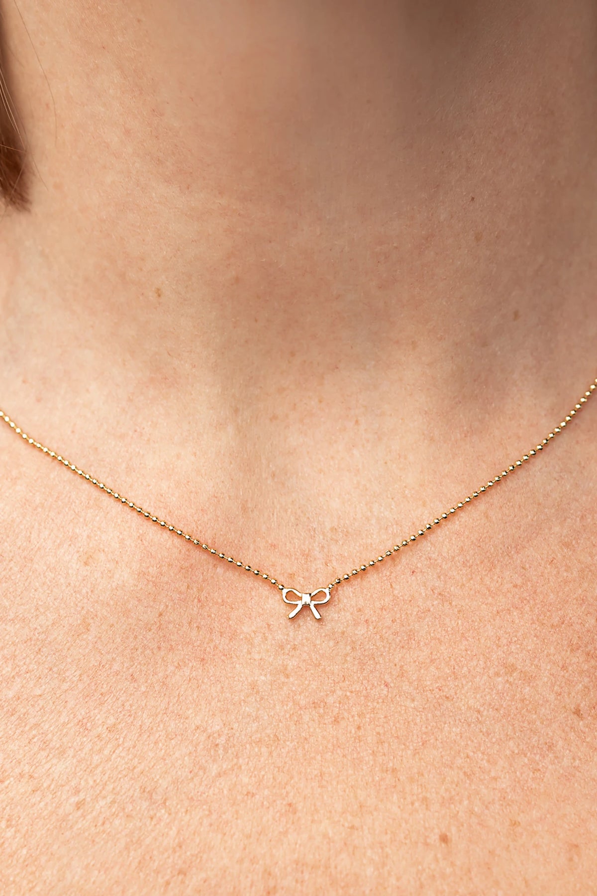 Holly Ribbon Bow Necklace in Gold with a dainty gold-tone chain and petite ribbon bow charm.