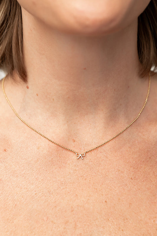 Holly Ribbon Bow Necklace in Gold with a dainty gold-tone chain and petite ribbon bow charm.