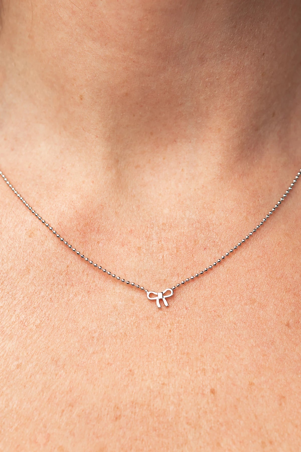 Holly Ribbon Bow Necklace in Silver with a dainty silver-tone chain and petite ribbon bow charm.