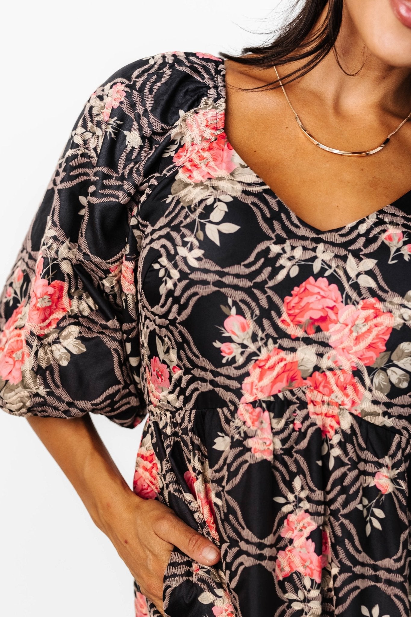 Close-up of embroidered pink floral pattern on matte black satin, showing texture and stitched detailing of the fabric.