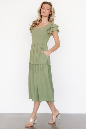 Front view of model wearing the Jacie Smocked Midi Dress in sage green with square neckline, smocked bodice, ruffle cap sleeves, and pockets, studio shot.