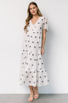 Three-quarter view highlighting navy floral embroidery and V-neckline on the Jesenia off-white midi dress, showing skirt drape.