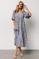 Model wearing Judith dress in blue with gold floral pattern showing oversized raglan balloon sleeves and elastic cuffs, side pockets visible.