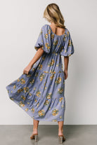 Styled shot of the Judith chiffon midi dress paired with simple accessories, emphasizing blue background that pulls purple and golden florals.