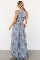 Back view of dusty blue floral tulle maxi dress on model, showing full lining, flowing skirt, and tank-style sleeve detail.