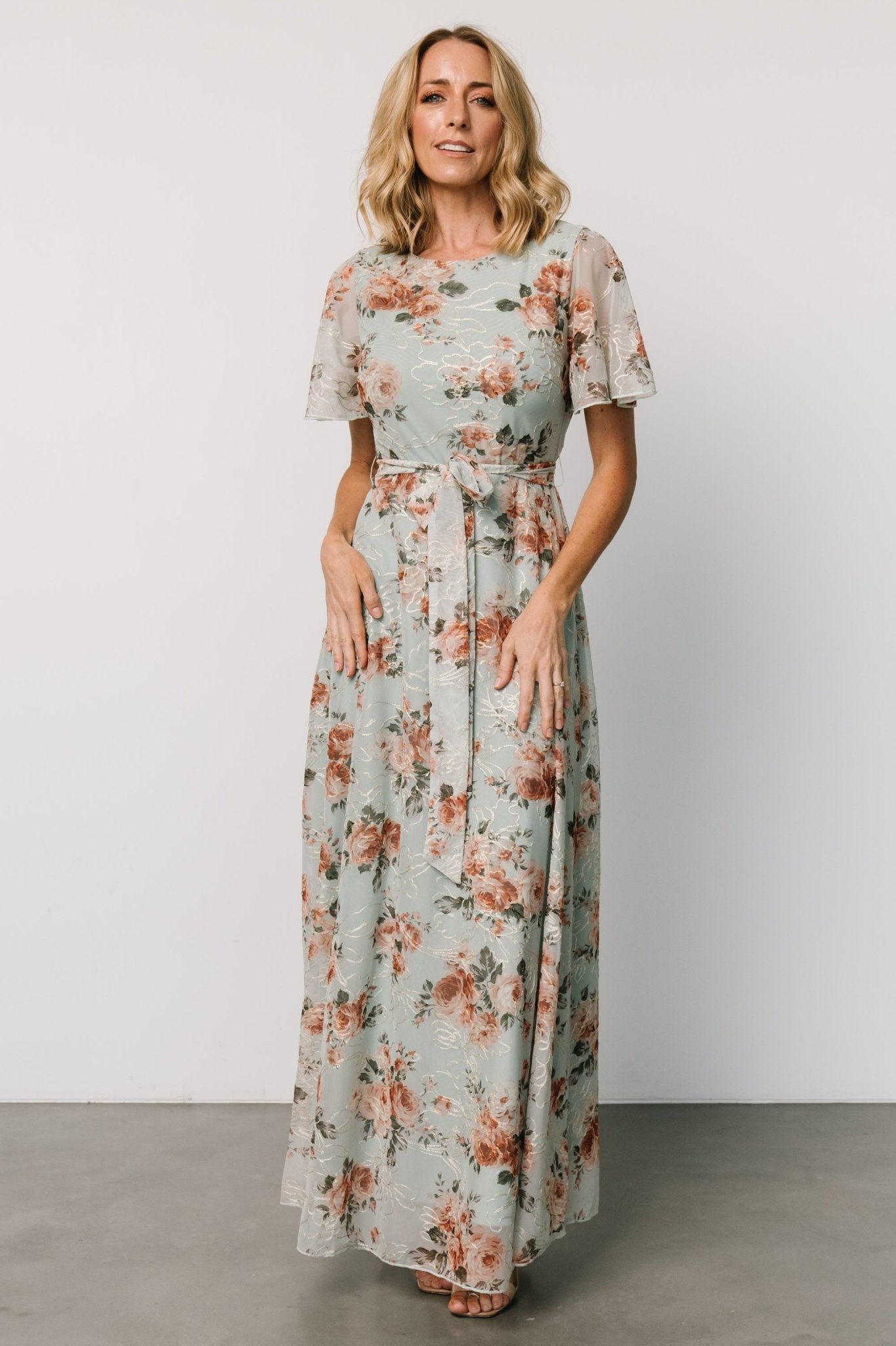 Model wearing Katalaya Maxi Dress in sage and gold, showing round neckline, keyhole back, elastic waist with self-tie sash, and embroidered tulle.