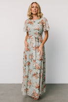 Model wearing Katalaya Maxi Dress in sage and gold, showing round neckline, keyhole back, elastic waist with self-tie sash, and embroidered tulle.