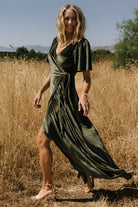 Back and movement shot of the velvet wrap maxi in dark olive, showing full lining, skirt flow, and sleeve length on model.