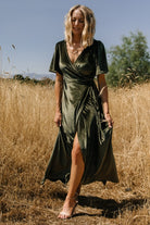 Front view of the Katelyn Velvet Maxi Wrap Dress in dark olive on a model, showing the V-neck, flutter sleeves, and tulip skirt in soft velvet.