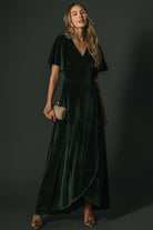 Front view of deep green velvet maxi wrap dress on model, showing higher-coverage V-neck, flutter sleeves, and tulip skirt (lined).