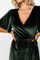 Model wearing the deep green wrap dress walking to show movement of the tulip-style skirt and flutter sleeves.