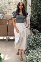 Side view of pleated midi skirt showing hidden side pocket, smooth drape, and the high-rise waistline on a standing model.
