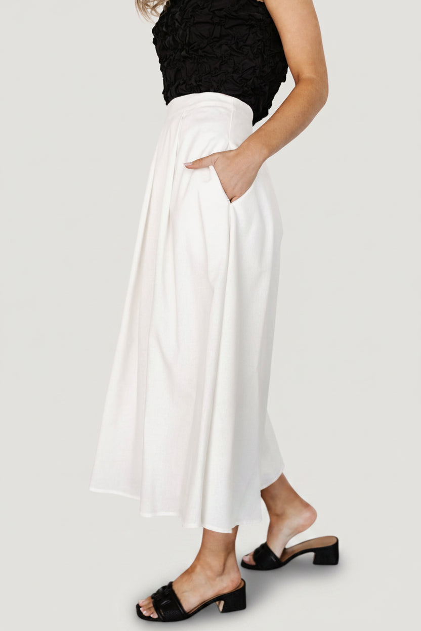 Back view of off-white pleated skirt highlighting the discreet back zipper, pleat fall, and finished hem at midi length.