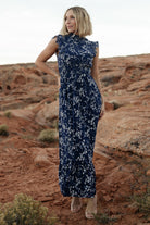 Front full-length view of blue floral chiffon maxi dress with smocked high neckline, short flutter sleeves, ruffle hem, and lined skirt on a model.