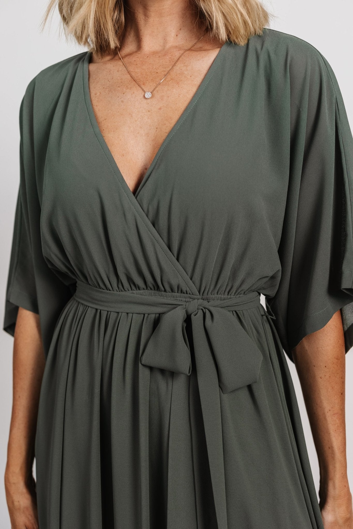 Side profile of dark sage Kia kimono maxi dress on model, highlighting left-side leg slit and graceful skirt movement.