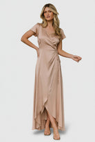 Front view of a model wearing the Krystal satin wrap gown in champagne, V-neckline, adjustable tie waist, floor-length tulip skirt and graceful drape.