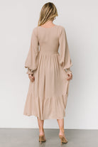 Detail shot of smocked sleeve cuff and elastic shoulder on a beige dotted midi dress, showing stitching and finish.