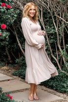 Beige dotted midi dress on model, smocked bodice, V-neck, long sleeves and tiered hem, front view with natural drape (model wearing dress).