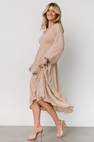 Full-length view of beige dotted midi dress on model, tiered hem and gentle drape from high V-waist to mid-calf.