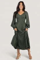 Detail image showing V‑neckline and elastic waist of the deep olive smocked dotted midi dress on a model.