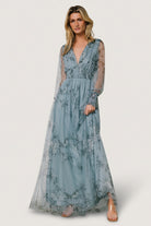 Three-quarter view showing the smocked waist detail and soft tulle overlay of the dusty blue floral maxi dress in motion.