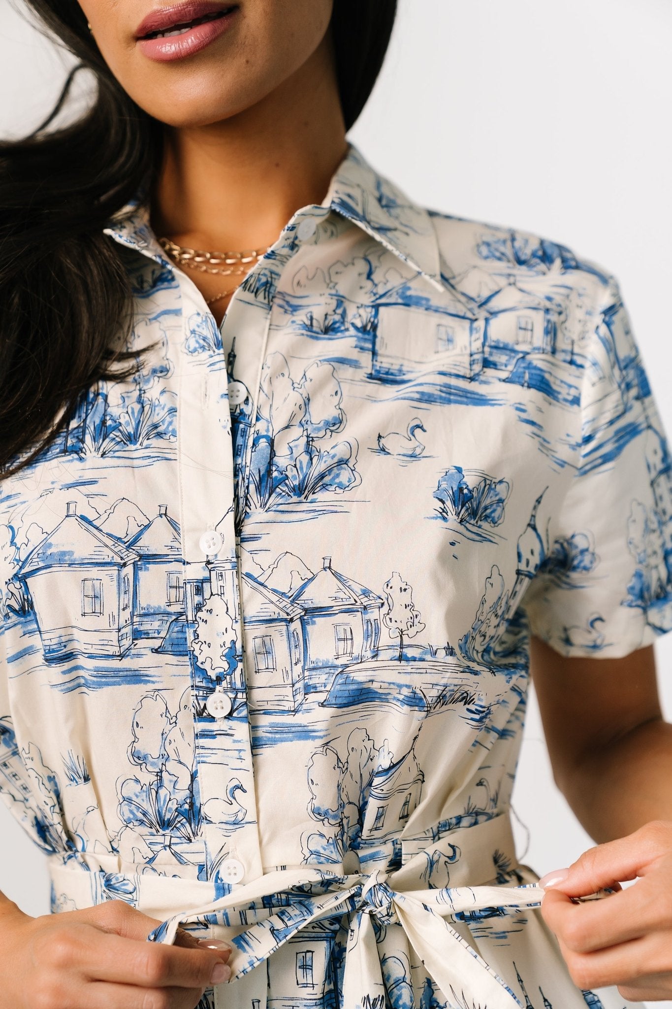 Three-quarter view on model showing midi length and short sleeves of the cream dress with delicate blue print and waist-defining self-tie belt.