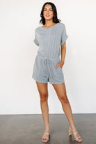 Model wearing the Lely romper in dusty blue — shows fit at the elastic waist, length, and how the faux tie and pockets sit when worn.