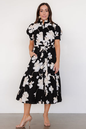 Front view of black Loewe button dress with off-white floral print, ruffle collar, removable sash, and tiered midi skirt, on model.