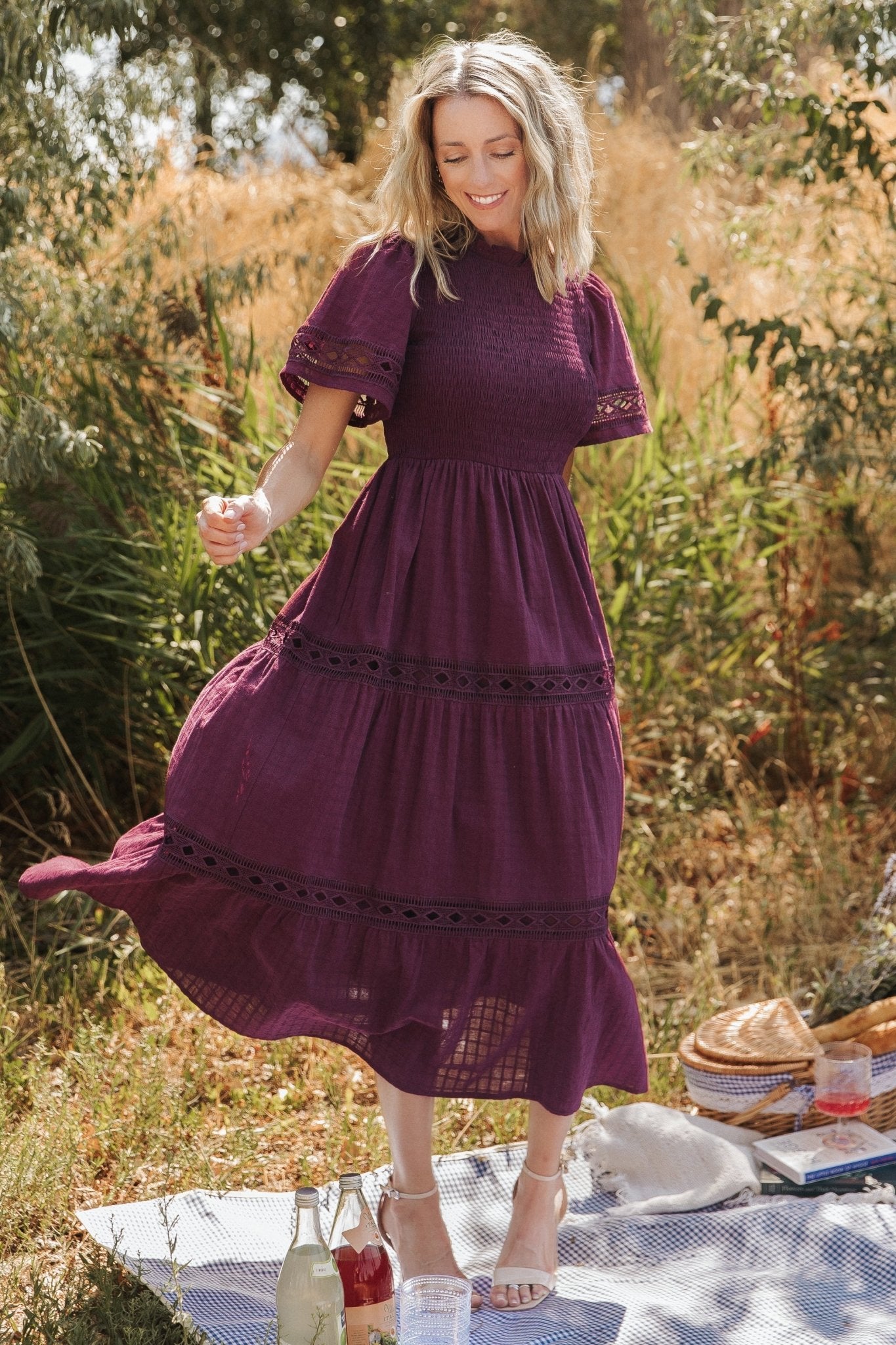 Front view of mulberry geo lace maxi dress showing ruffled round neckline, smocked bodice, and tiered skirt in motion, with pockets visible.