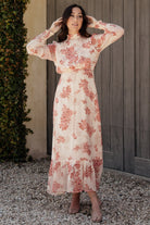 Front view of Luciana maxi dress in beige and rose floral, showing smocked high neckline, long ruffle sleeves, pleated front waist, and tiered maxi hem.