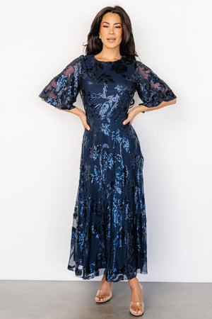 Front view of navy tulle maxi dress with monochromatic floral sequin pattern, round neckline, and flowing raw-hem skirt (full-length).