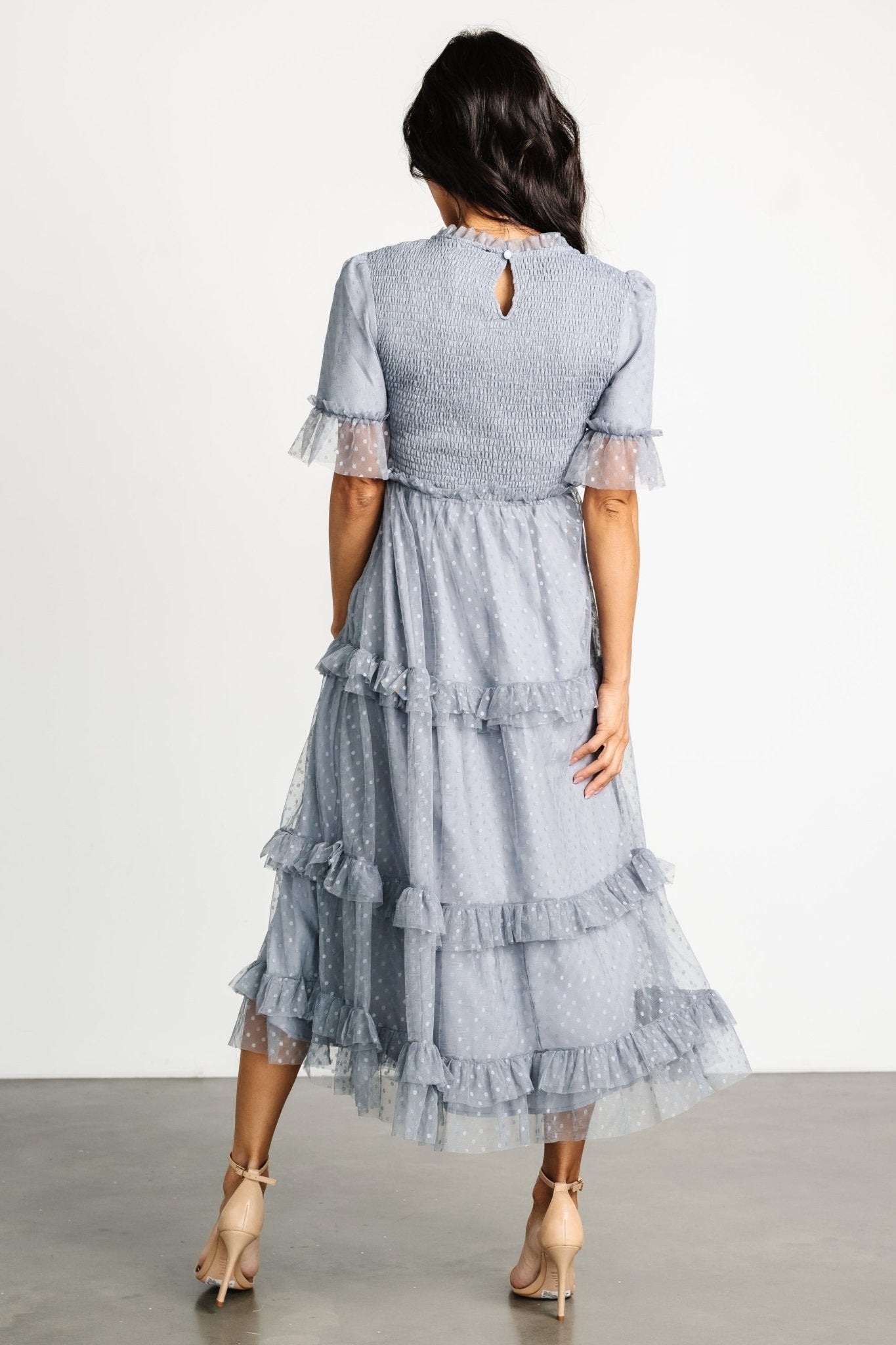 Full-length shot of Lysandra smocked dot midi dress in dusty slate showing movement of tiered skirt and ruffle detailing on sleeves and hem.
