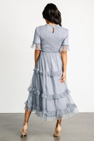 Full-length shot of Lysandra smocked dot midi dress in dusty slate showing movement of tiered skirt and ruffle detailing on sleeves and hem.