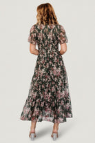 Model wearing dark green embroidered tulle midi dress, showing overall fit, smocked bodice, ankle-length tiers, and floral details.