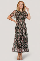 Front view of dark green embroidered tulle midi dress with blush and berry florals, showing smocked bodice and flutter sleeves.