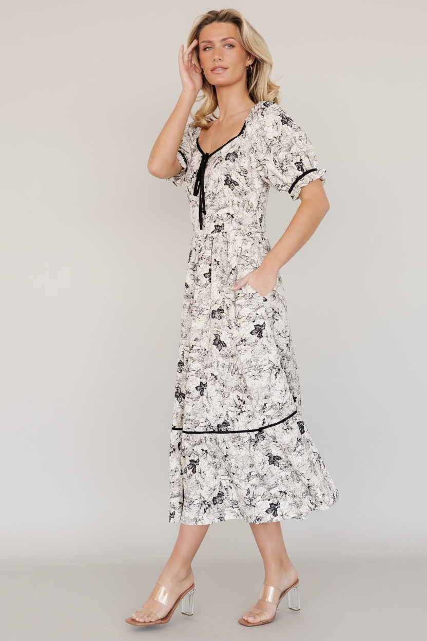 Back view of dress highlighting smocked back, elastic ruffled sleeve hems, and the single-tiered skirt silhouette in cream and black floral.