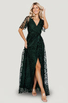 Full-length front view of dark green vine-embossed maxi dress with surplice neckline, elastic waistband, self-tie, and left-leg slit on a model.