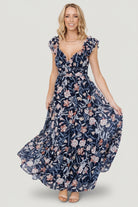 Front model view of Martina Maxi Dress in navy multi floral chiffon, showing V-neck, gathered bust, and flowing tiered skirt; model wearing size S.