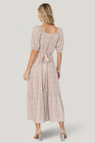 Back view of a beige floral maxi dress displaying smocked panel, adjustable back tie, and the flow of the single-tier skirt for fullness.
