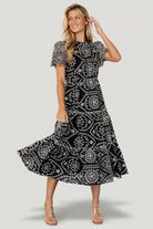 Front view of Mirabel embroidered eyelet midi dress in black with white floral embroidery, ruffled high neckline and scalloped short sleeves.