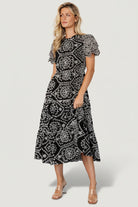 Model wearing Mirabel Eyelet Midi Dress in black and white, showing fit at waist, tiered skirt length and overall silhouette for styling.
