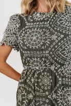 Back view showing keyhole-and-button closure, elasticated waist, and tiered skirt on the Mirabel Eyelet Midi Dress in olive and white.