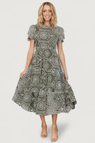 Model wearing Mirabel Eyelet Midi Dress in olive and white, showing fit at the waist, lined bodice, and midi length.