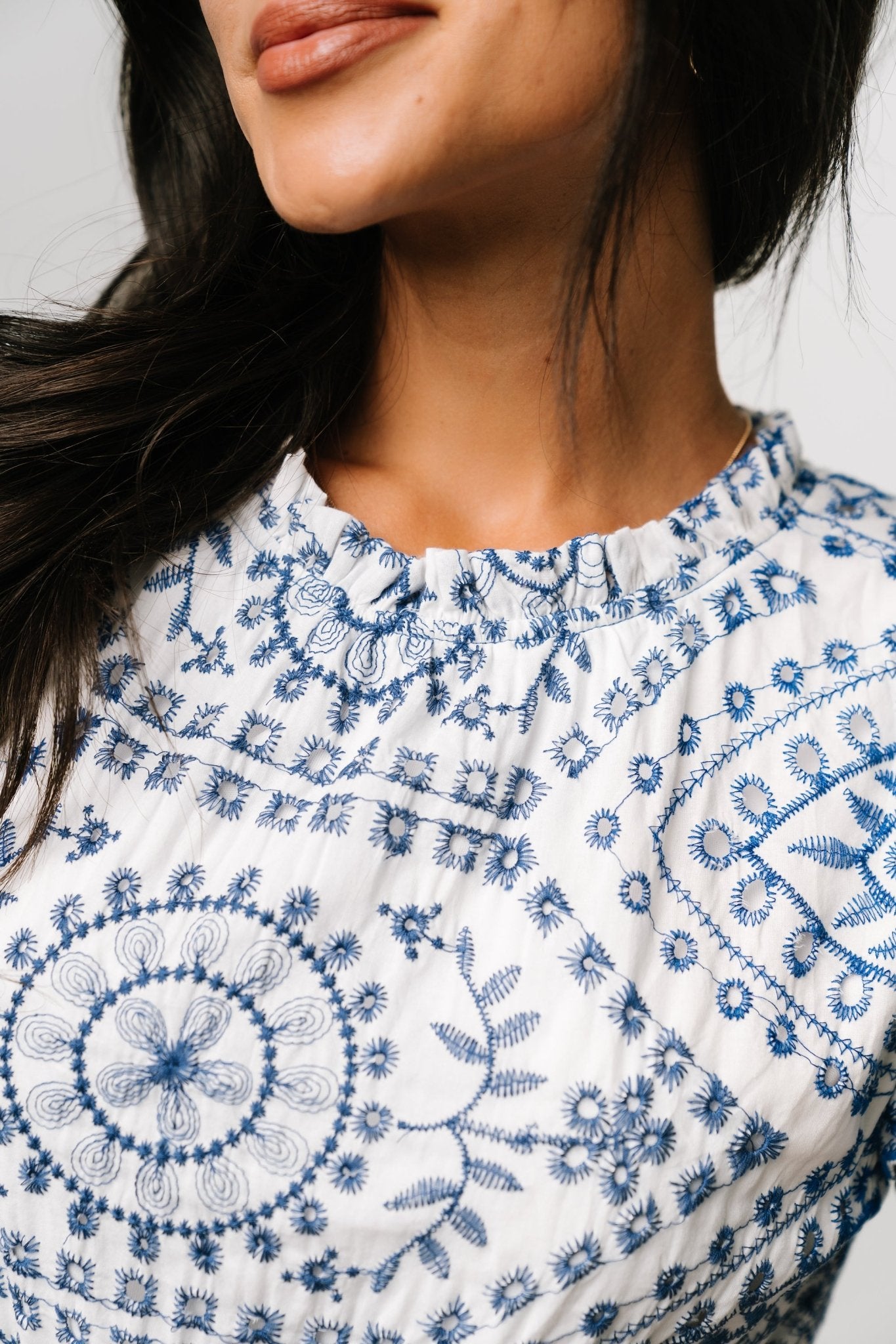 Close-up of blue embroidered eyelet detailing and scalloped edge on the short layered sleeve of the white midi dress.