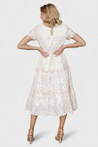 Back view highlighting the keyhole button closure at the neckline, ruffle trim, and how the tiers fall on the white embroidered midi dress.