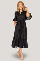 Back view of the black Mirielle midi dress showing the skirt silhouette, gathered tier, and length hitting mid-calf.