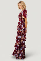 Model wearing mulberry floral maxi dress walking to show ruffle movement, short sleeves and the dress’s overall flattering, flowing silhouette.