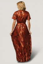 Model wearing Muse Sequin Maxi Dress in cinnamon with sequin leaf accents, styled with minimal jewelry to showcase the dress's shimmer and silhouette.