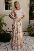 Back view showing the keyhole and button closure at the nape, short sheer sleeves, and the flowing maxi skirt with consistent rose-gold sequin embellishment.