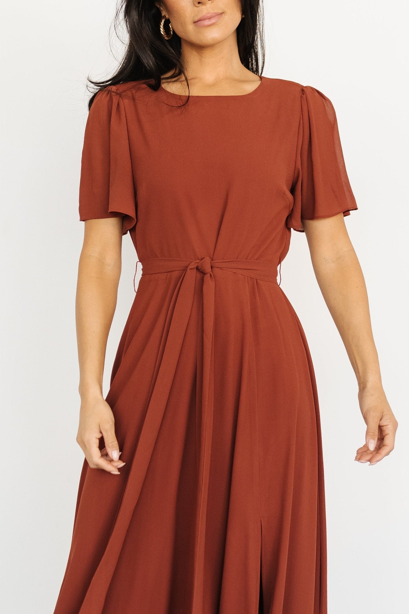 Three-quarter view of Naomi cinnamon chiffon maxi dress demonstrating the removable belt tie and maxi-length sweep.
